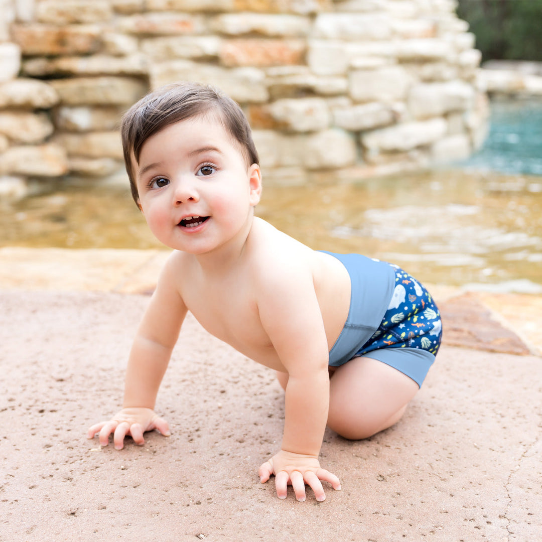 Little one wearing neoprene swim nappy in blue, featuring sharks themed print. 