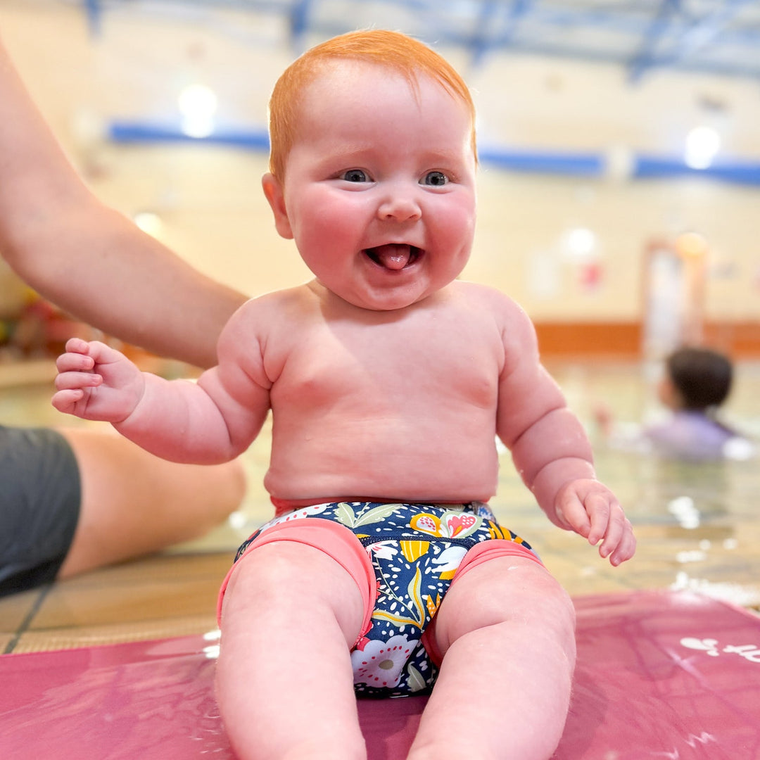 Little one wearing neoprene swim nappy in navy with pink trims, and floral themed print.