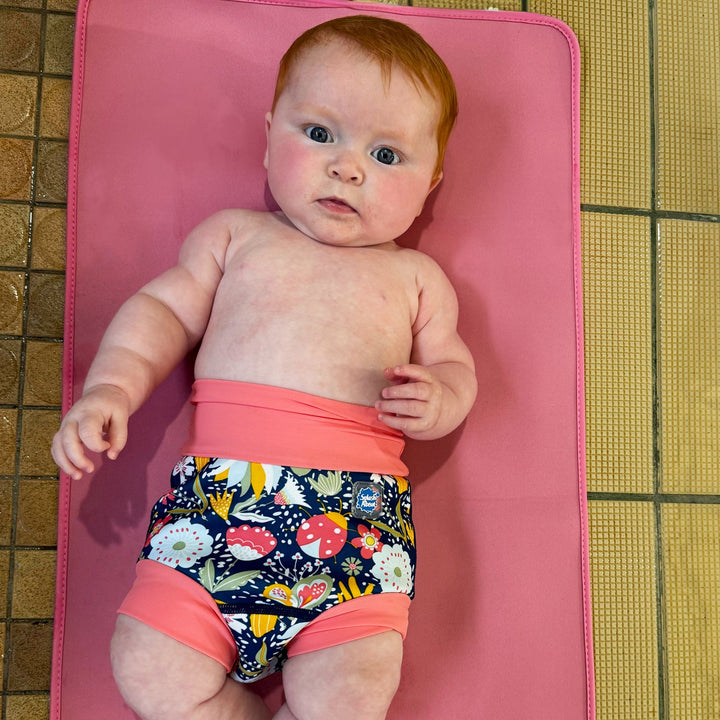 Little one wearing neoprene swim nappy in navy with pink trims, and floral themed print.