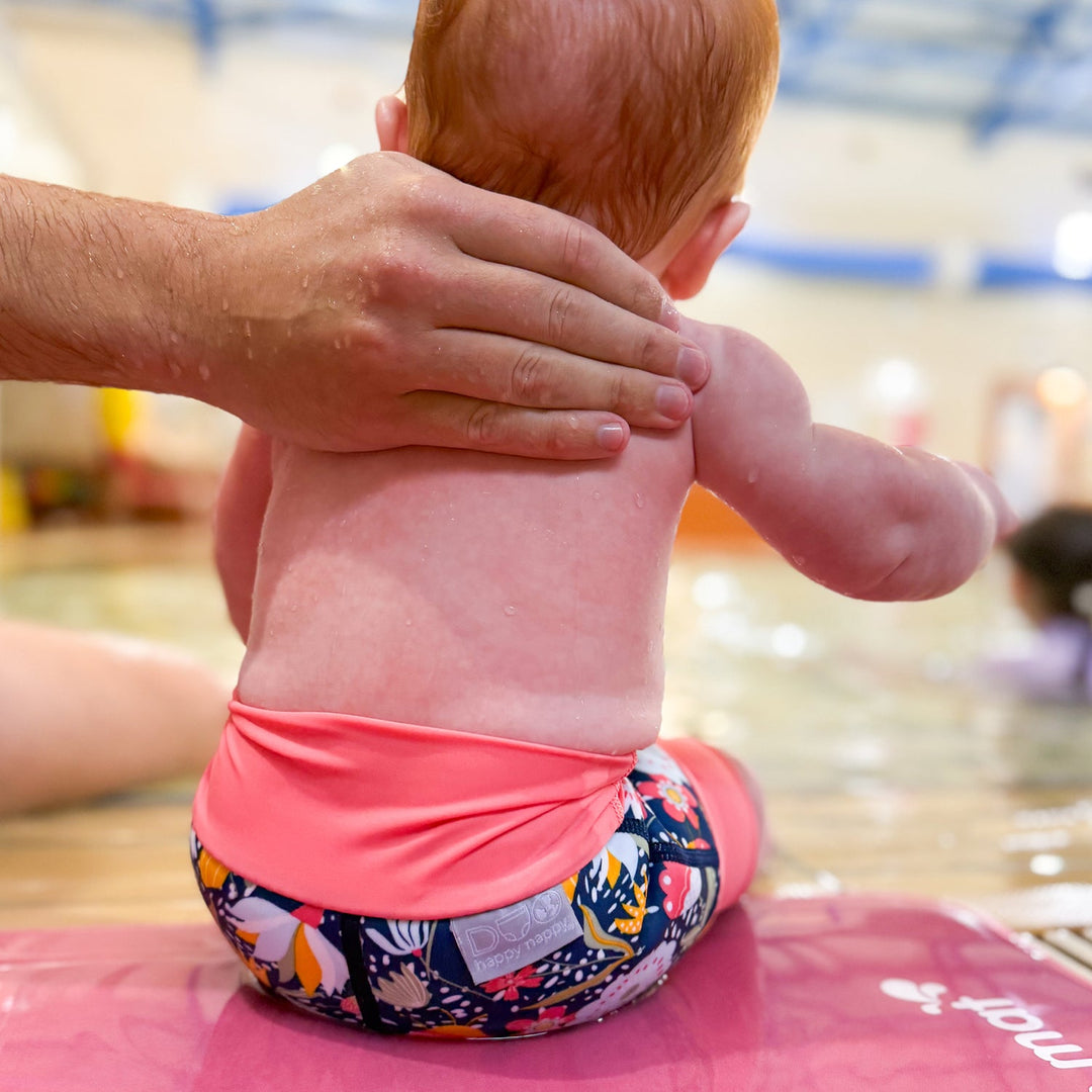 Little one wearing neoprene swim nappy in navy with pink trims, and floral themed print.