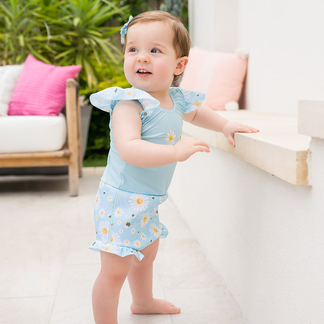 Little one wearing Happy Nappy Costume in light blue and daisies and bees themed print, featuring frills in arms and legs.