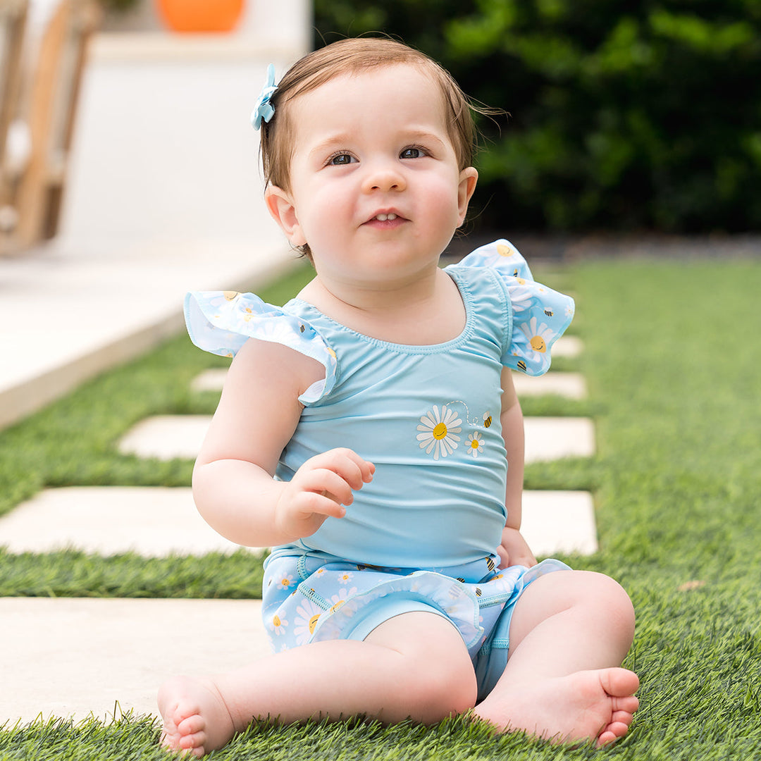 Little one wearing Happy Nappy Costume in light blue and daisies and bees themed print, featuring frills in arms and legs.