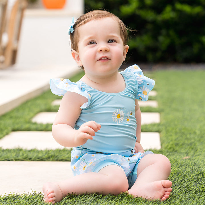 Little one wearing Happy Nappy Costume in light blue and daisies and bees themed print, featuring frills in arms and legs.