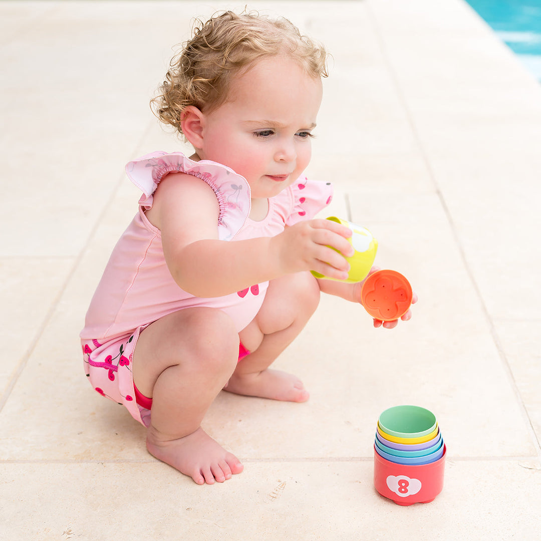 Little one wearing Happy Nappy Costume in pink and cherries themed print, featuring frills in arms and legs.