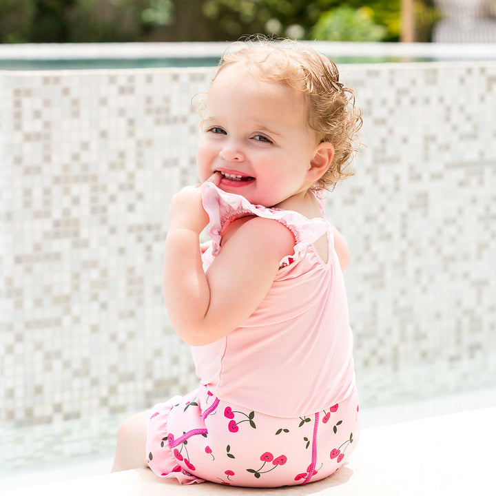 Little one wearing Happy Nappy Costume in pink and cherries themed print, featuring frills in arms and legs.
