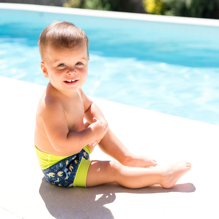 Little one wearing neoprene swim nappy in navy, with lime ribs and turtles themed print.