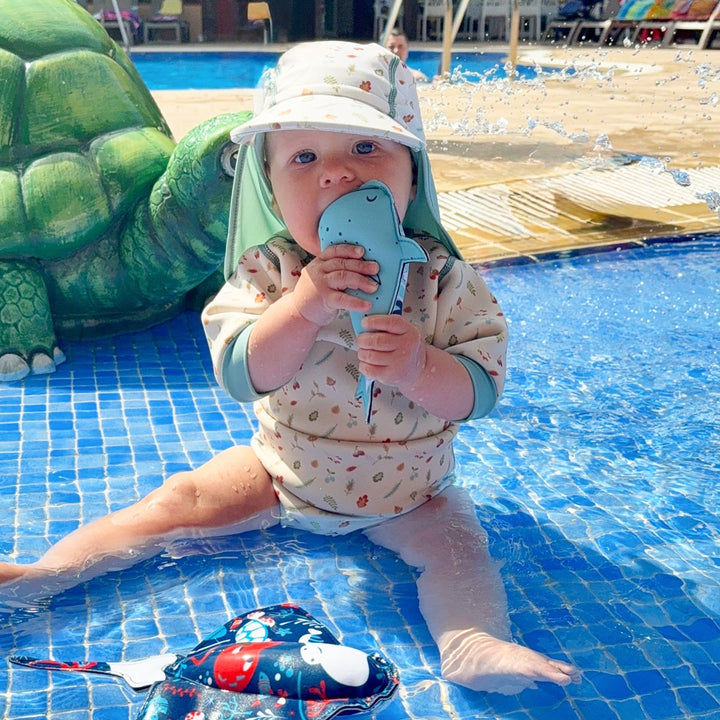Lifestyle image of child wearing baby wetsuit with built in swim nappy in white with light blue trims and leaves and acorns themed print.