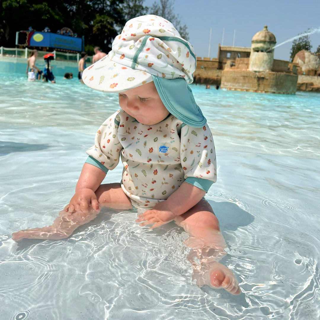 Lifestyle image of child wearing baby wetsuit with built in swim nappy in white with light blue trims and leaves and acorns themed print.