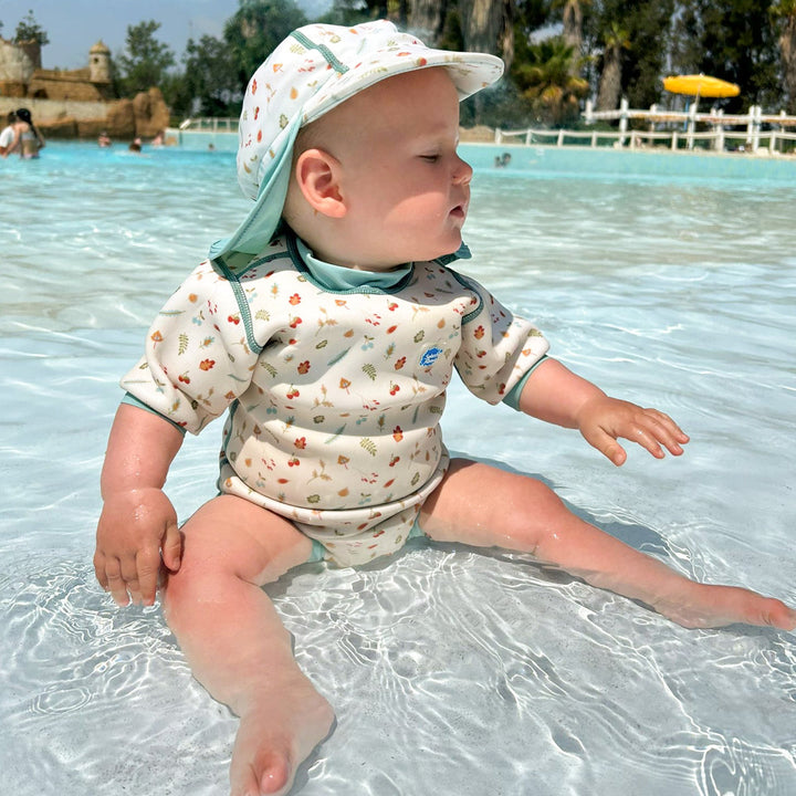 Lifestyle image of child wearing baby wetsuit with built in swim nappy in white with light blue trims and leaves and acorns themed print.