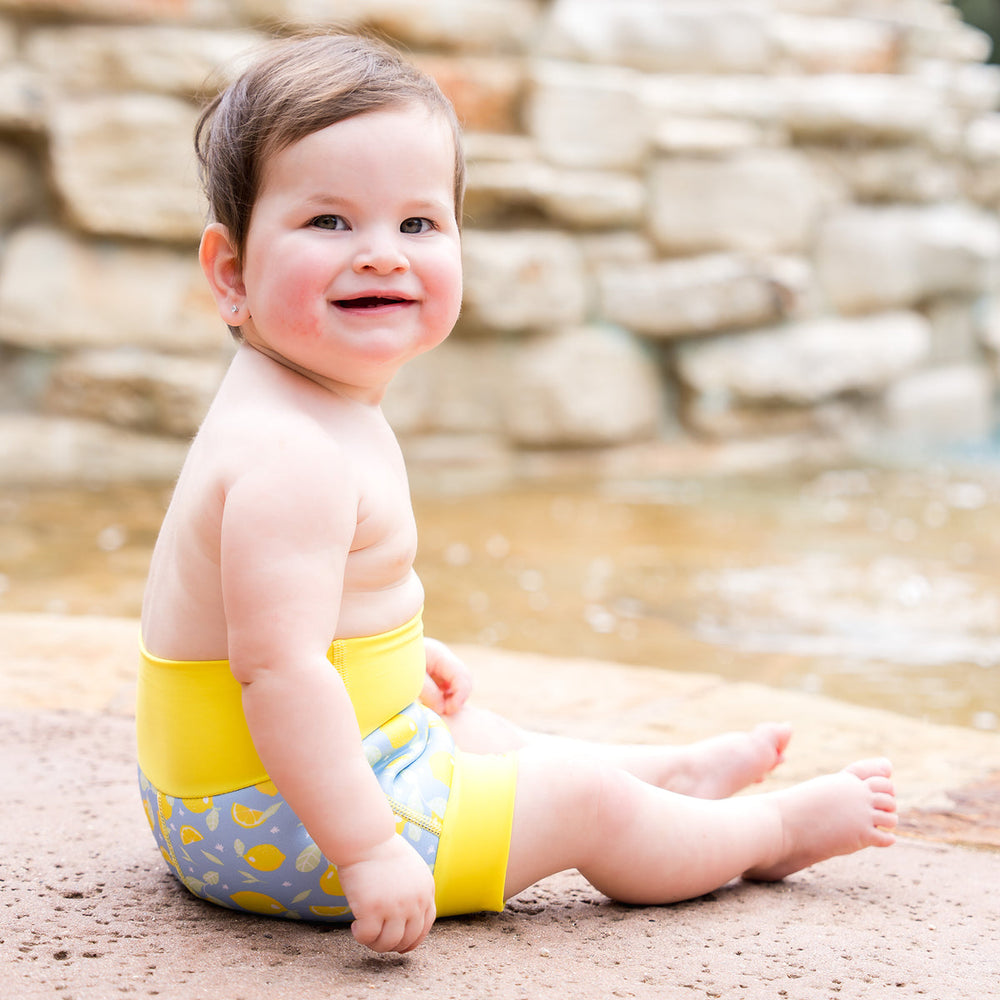 Little one wearing neoprene swim nappy in blue, with yellow ribs and lemons themed print.