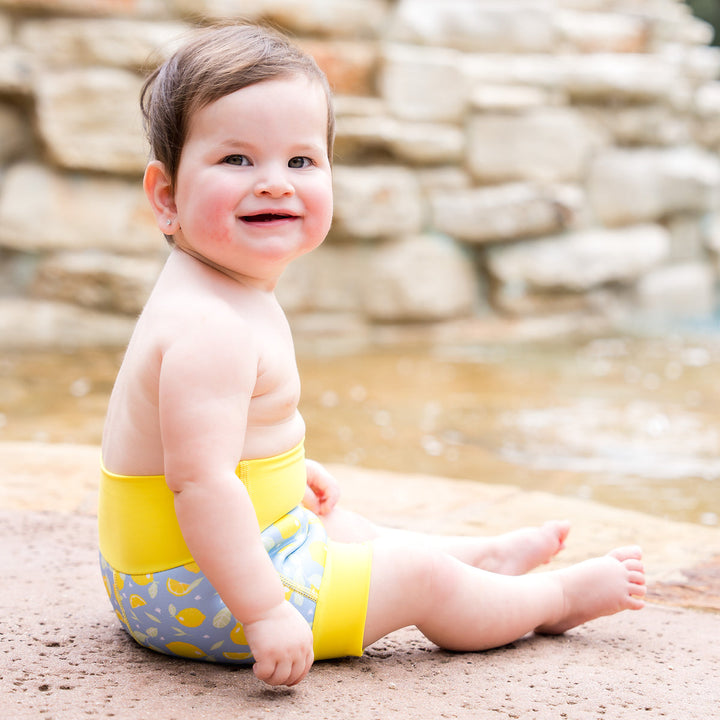 Little one wearing neoprene swim nappy in blue, with yellow ribs and lemons themed print.