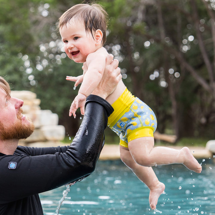 Little one wearing neoprene swim nappy in blue, with yellow ribs and lemons themed print.