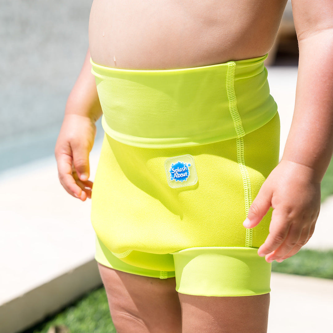 Close up of little one wearing neoprene swim nappy in bright lime green, front.