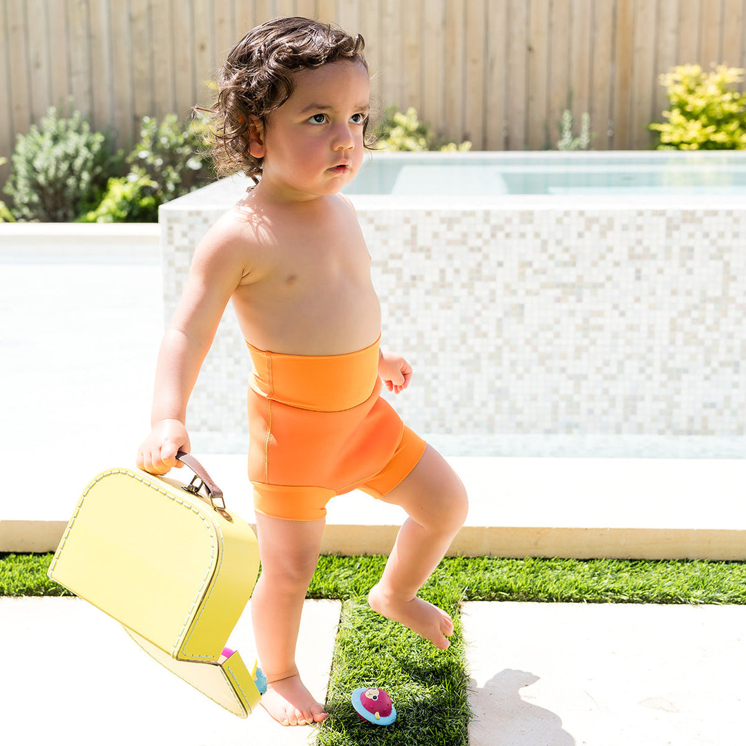 Little one wearing neoprene swim nappy in bright orange, poolside.