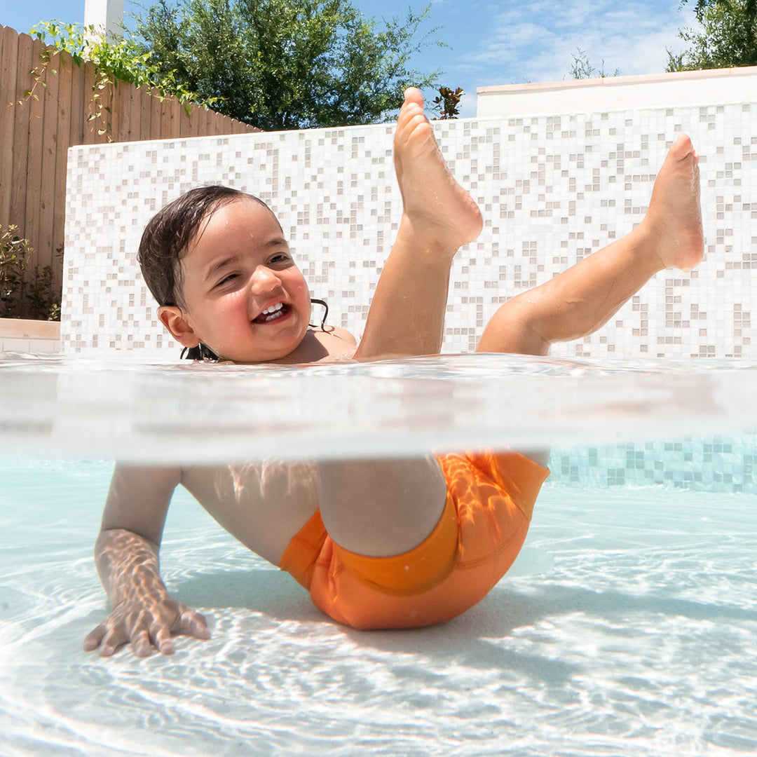 Little one swimming in neoprene swim nappy in bright orange.