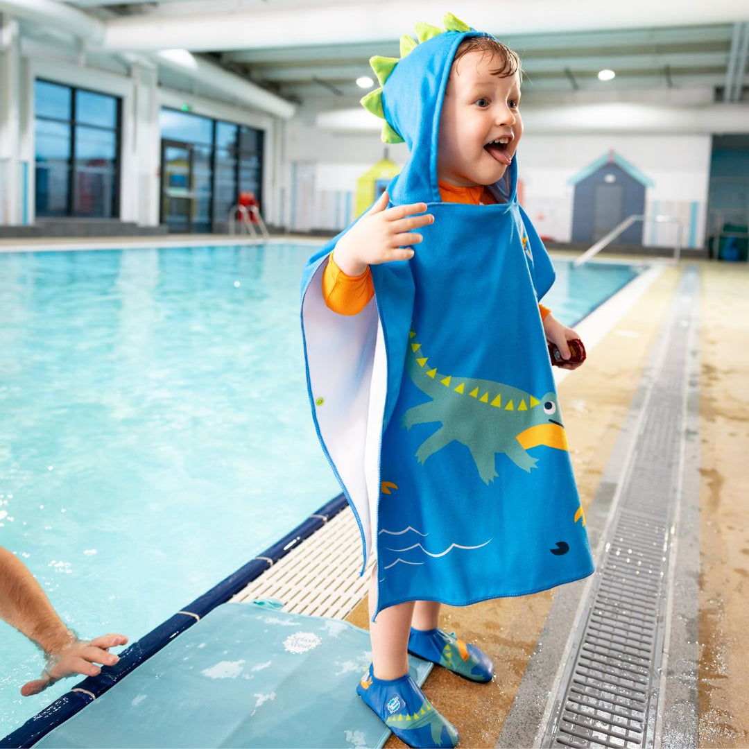 Little one wearing poncho towel in blue with crocodiles and frogs themed print.