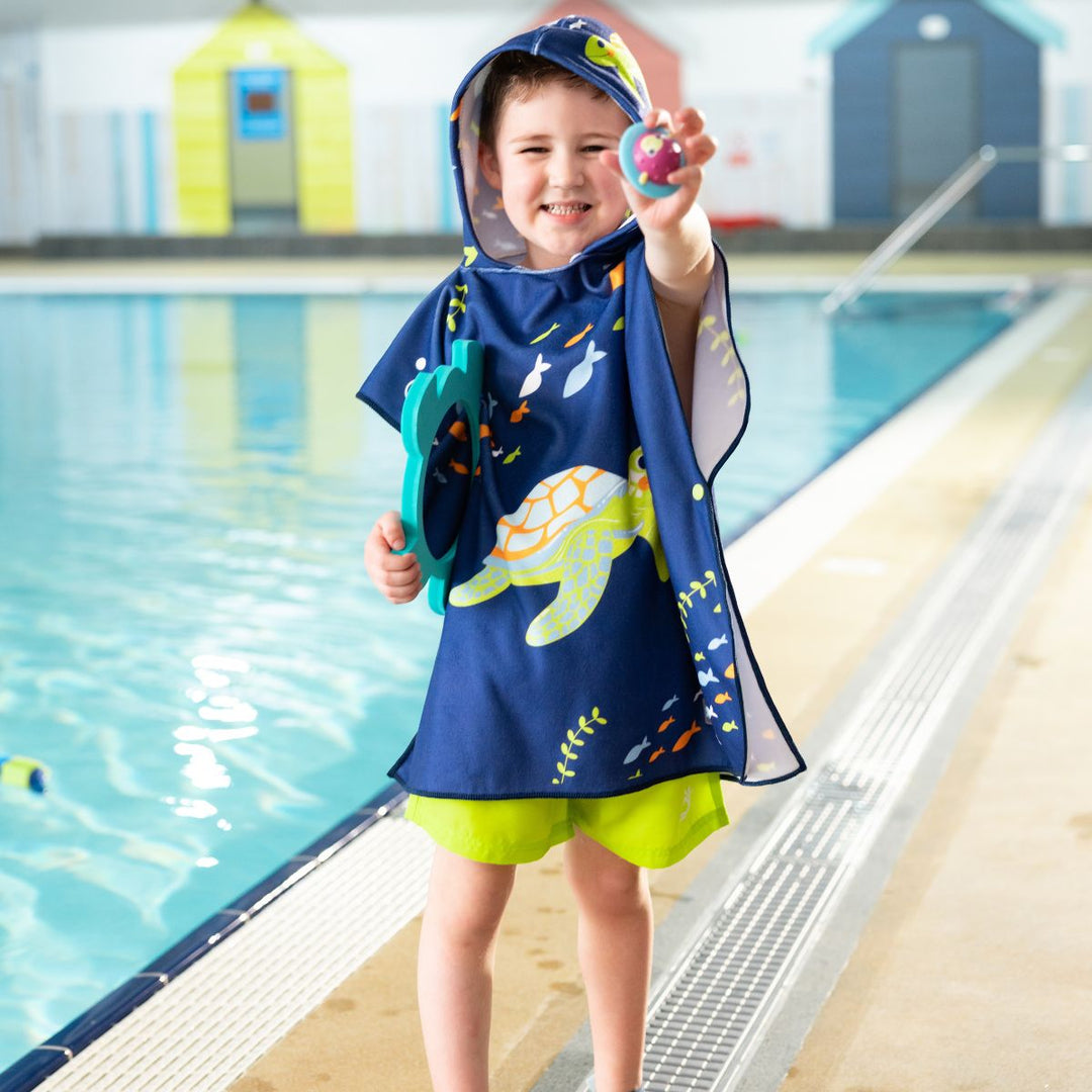 Little one wearing hooded poncho in navy with turtles and sea creatures themed print.