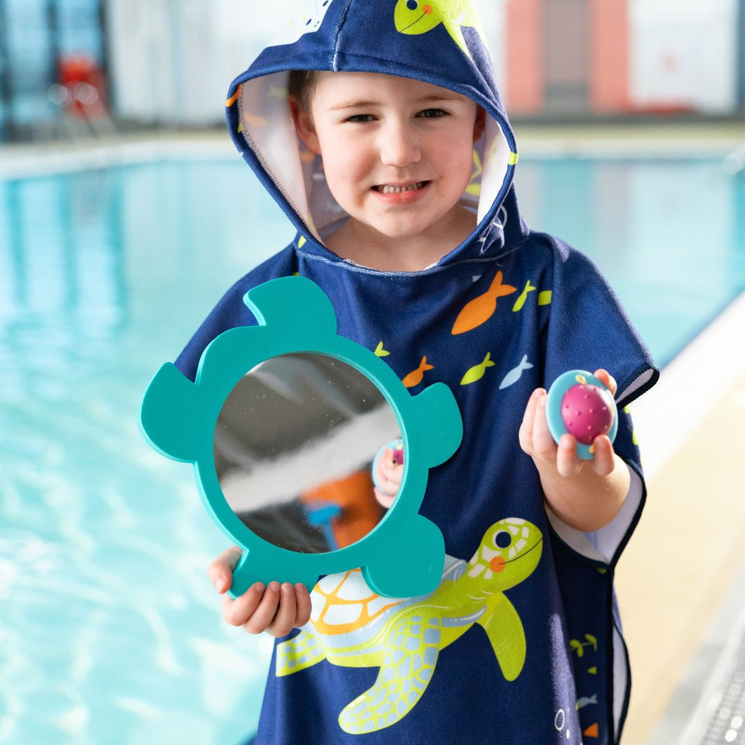 Little one wearing hooded poncho in navy with turtles and sea creatures themed print.