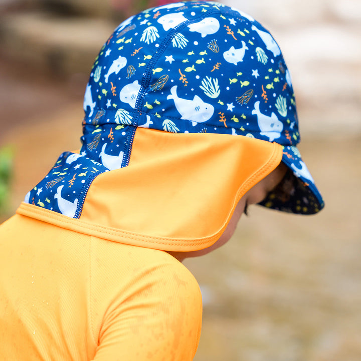 Little one wearing legionnaire style sun hat in navy and orange, with sharks themed print panel.
