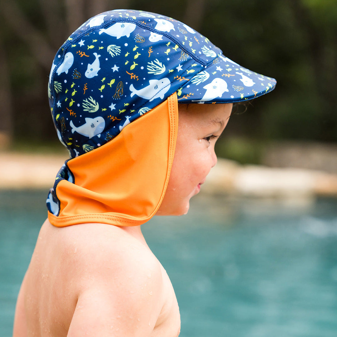 Little one wearing legionnaire style sun hat in navy and orange, with sharks themed print panel.