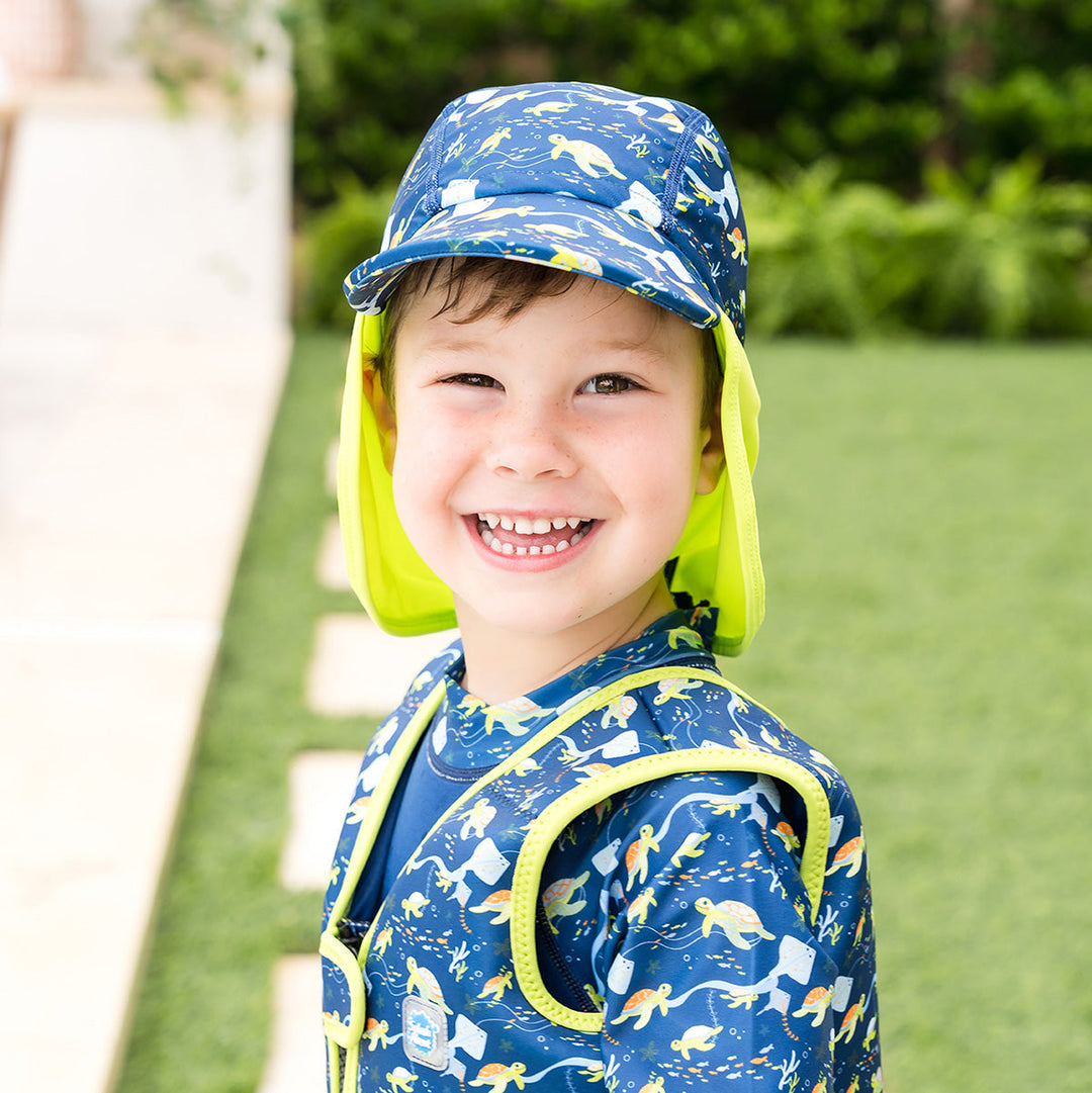 Little one wearing legionnaire style sun hat in navy and lime, with turtles and mantarays themed print panel. They are also wearing matching swim vest.