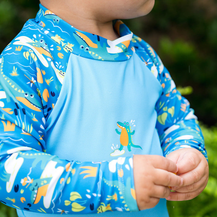 Close-up of little one wearing UV protective long sleeve rash top in blue, featuring crocodiles and frogs themed print on the chest and sleeves.