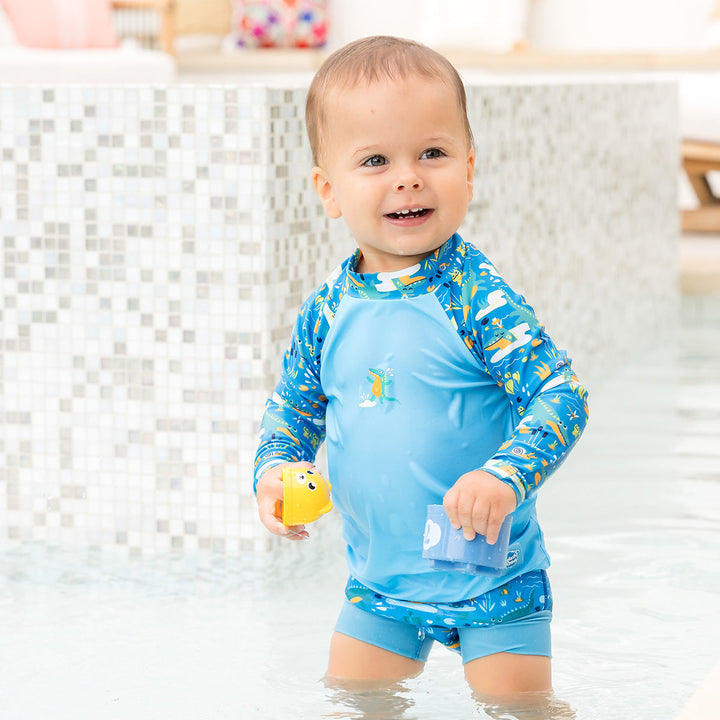 Little one wearing UV protective long sleeve rash top in blue, featuring crocodiles and frogs themed print on the chest and sleeves. They are also wearing matching Happy Nappy.