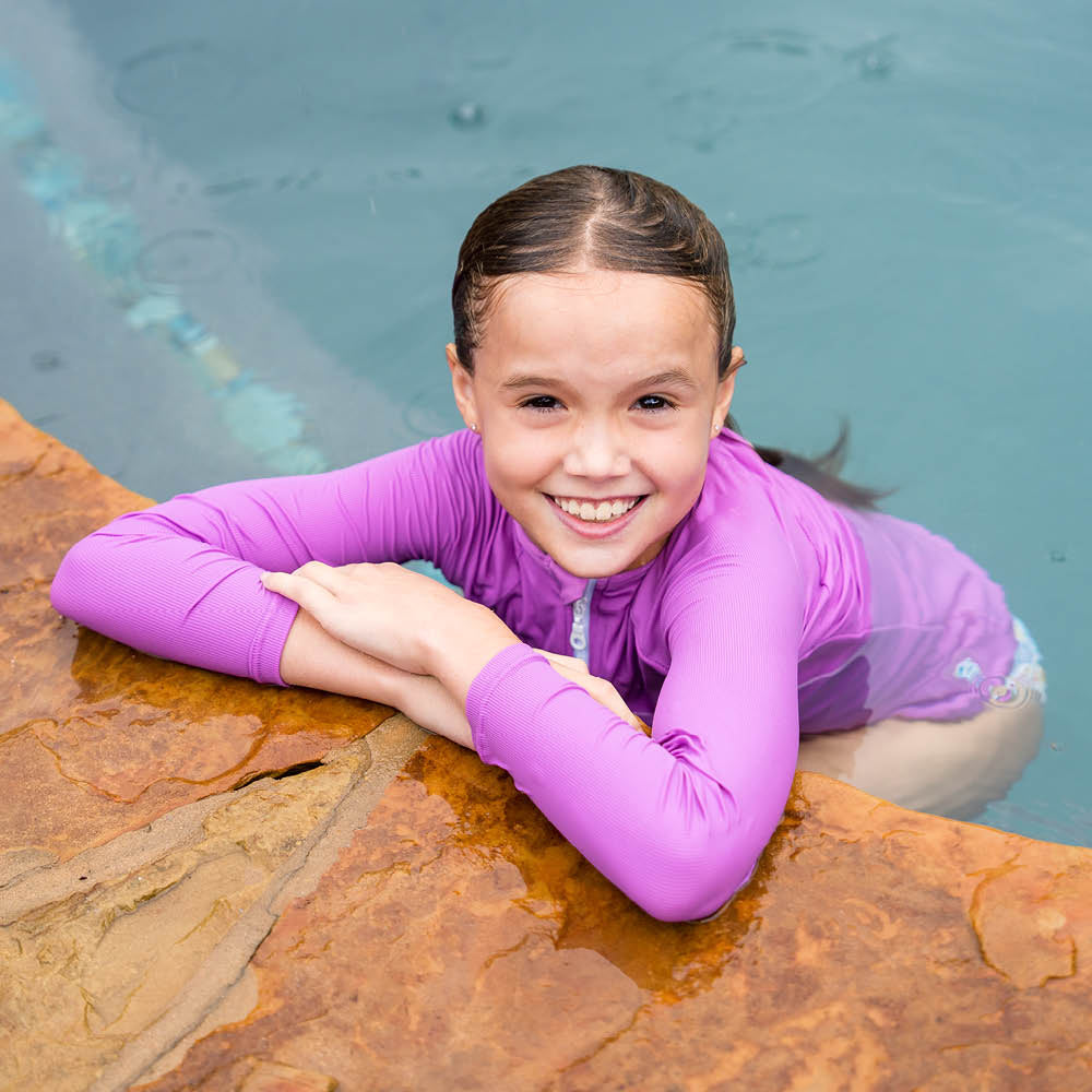 Older child wearing UV protective long sleeve rash top in lilac, over regular swimwear.