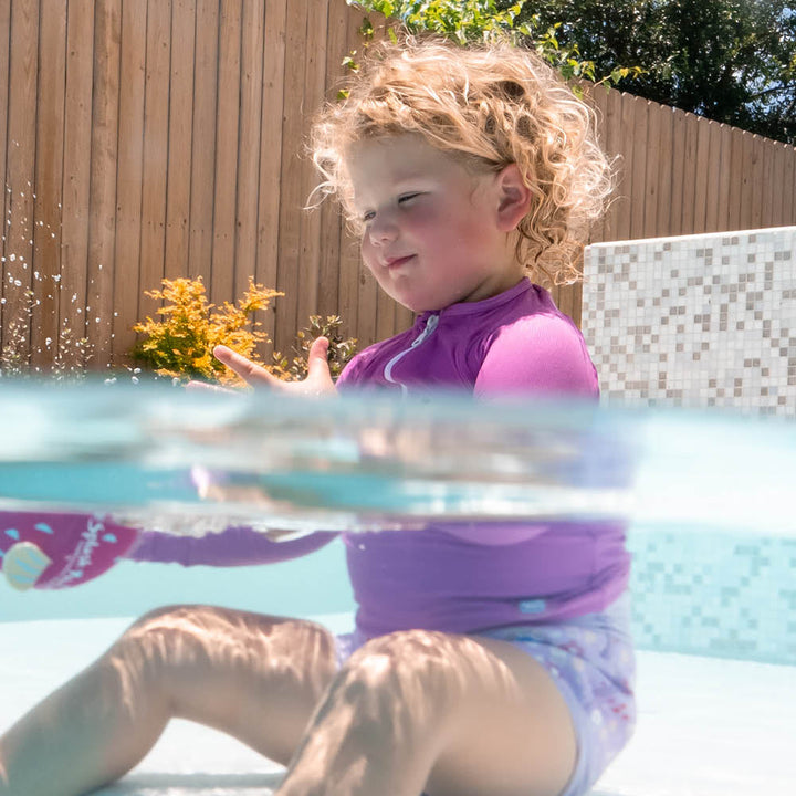 Little one wearing UV protective long sleeve rash top in lilac. They are also wearing lilac Happy Nappy.