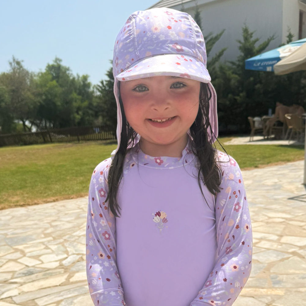 Little one wearing protective long sleeve rash top in lilac, and floral themed print on the chest and sleeves. They are also wearing matching Legionnaire Hat.