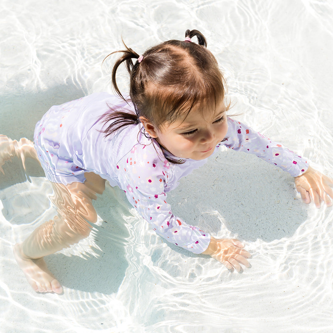 Little one swimming in protective long sleeve rash top in lilac, and floral themed print on the chest and sleeves.