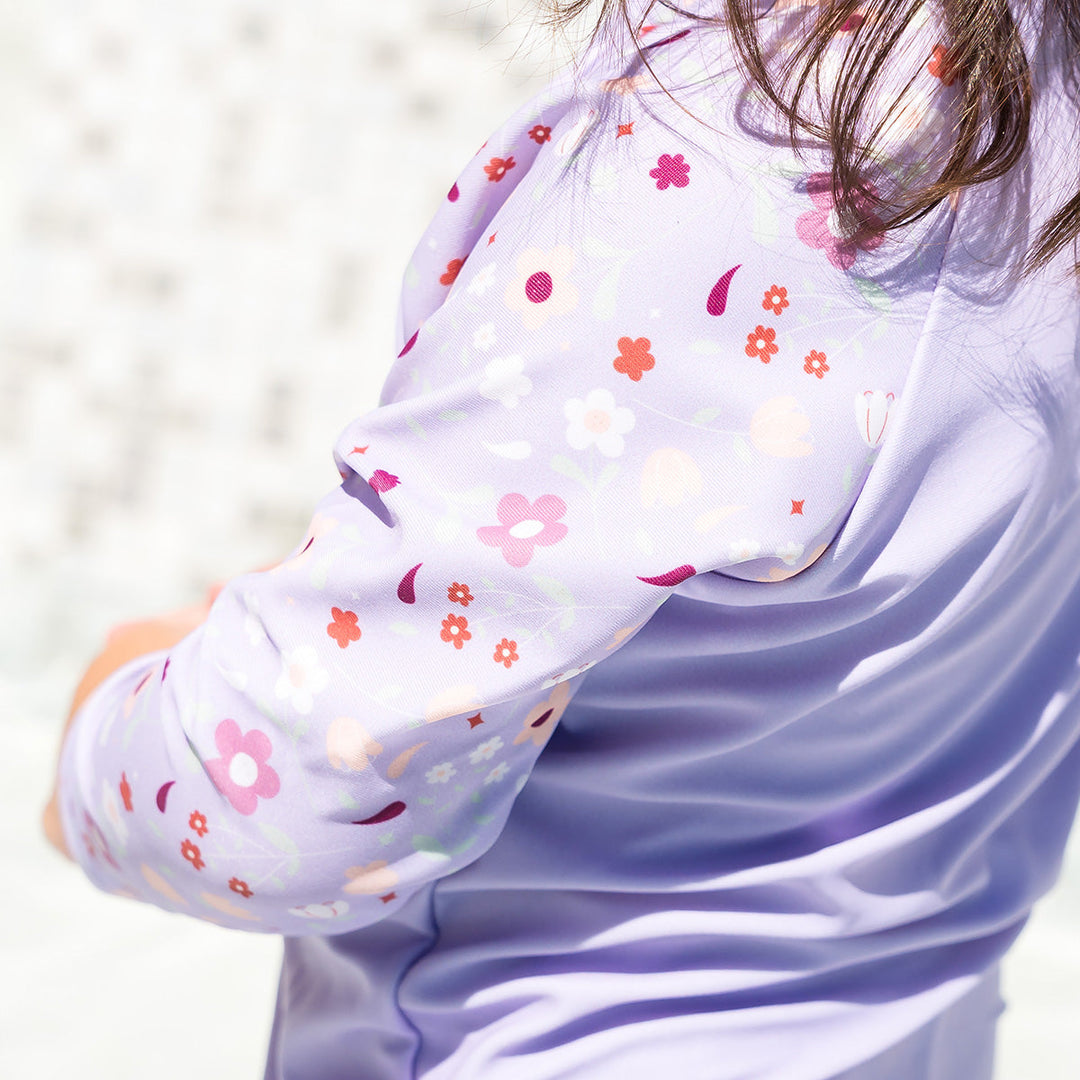 Close up of little one wearing protective long sleeve rash top in lilac, and floral themed print on the chest and sleeves..