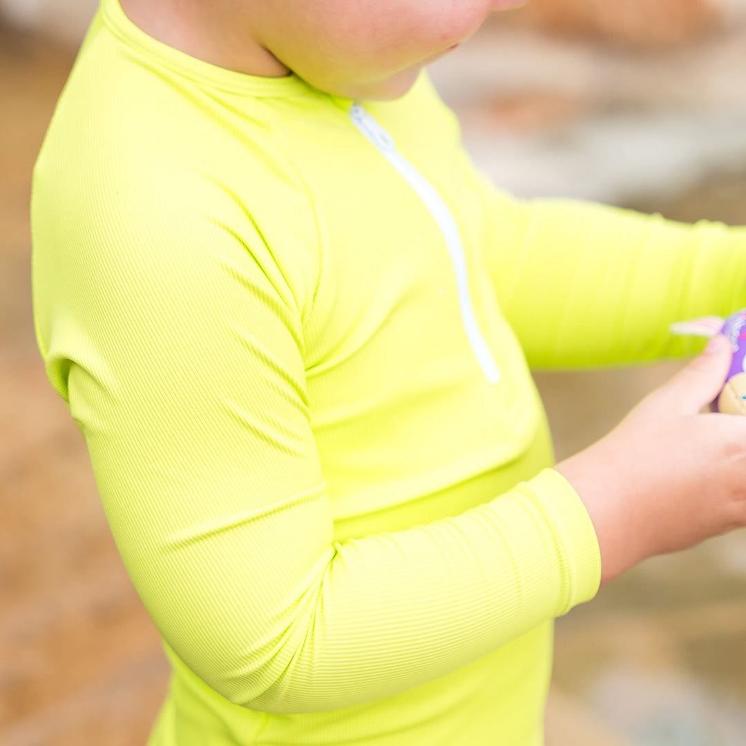 Close-up of little one wearing UV protective long sleeve rash top in neon green/yellow.