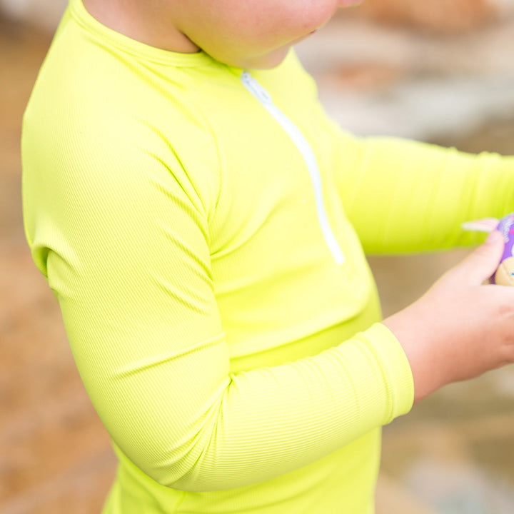 Close-up of little one wearing UV protective long sleeve rash top in neon green/yellow.