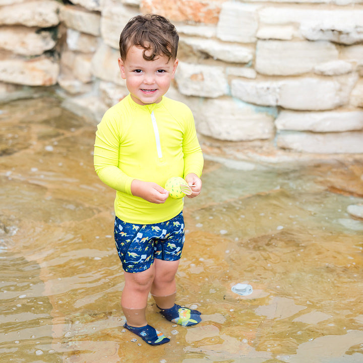 Little one wearing UV protective long sleeve rash top in neon green/yellow. They are also wearing blue jammers.
