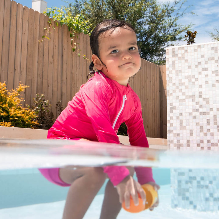 Little one wearing UV protective long sleeve rash top in neon pink. They are also wearing neon pink Happy Nappy.