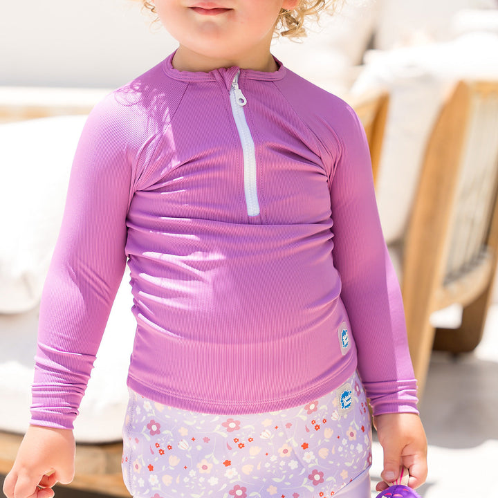 Close-up of little one wearing UV protective long sleeve rash top in lilac. They are also wearing lilac Happy Nappy.