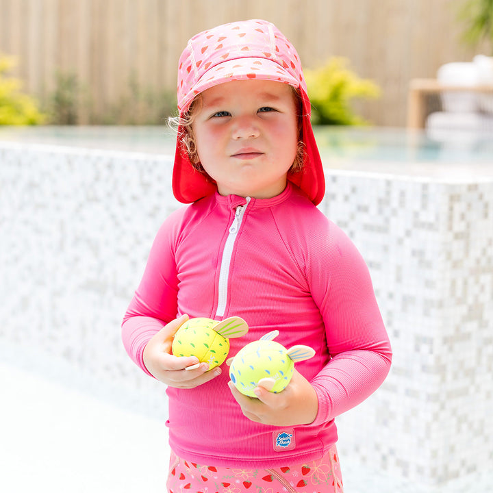 Little one wearing UV protective long sleeve rash top in neon pink. They are also wearing pink jammers and matching legionnaire hats.