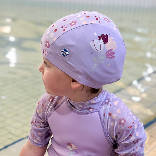 Little one wearing baby swim hat in lilac featuring floral themed print.