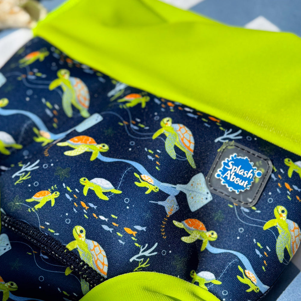 Little one wearing neoprene swim nappy in navy, with lime ribs and turtles themed print.