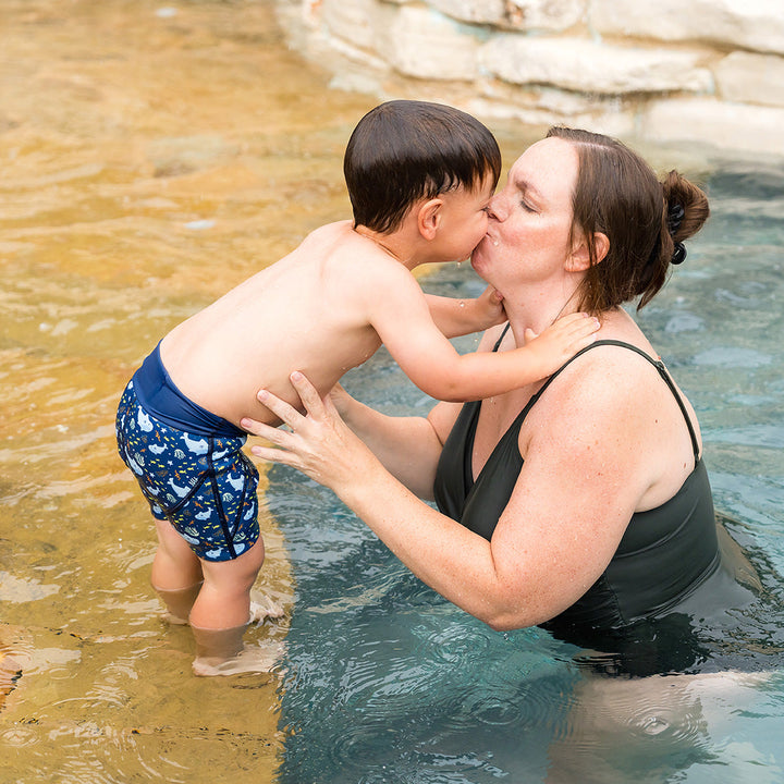 Child wearing neoprene swim shorts in navy and sharks themed print.