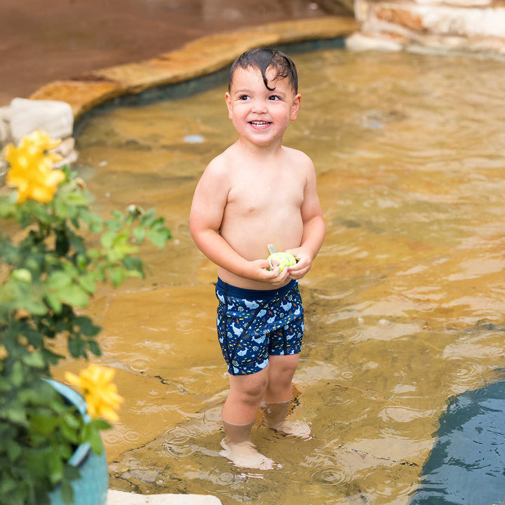 Child wearing neoprene swim shorts in navy and sharks themed print.