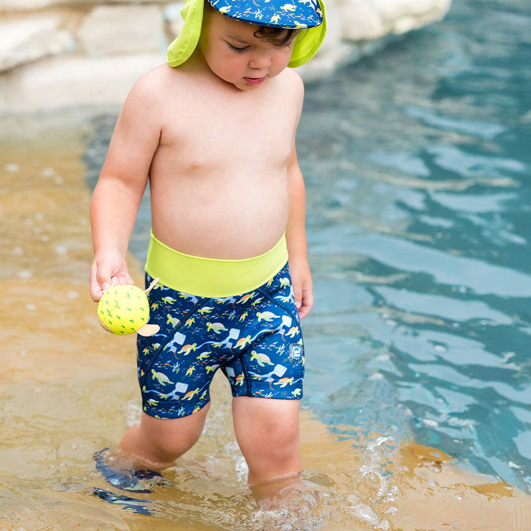 Child wearing neoprene swim shorts in navy and turtles and mantrays themed print.