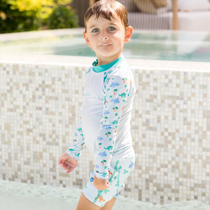 Child wearing neoprene swim shorts in mint and dinosaurs themed print. He&