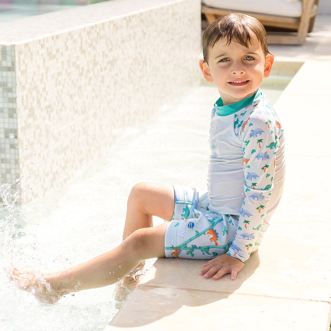 Child wearing neoprene swim shorts in mint and dinosaurs themed print. He&