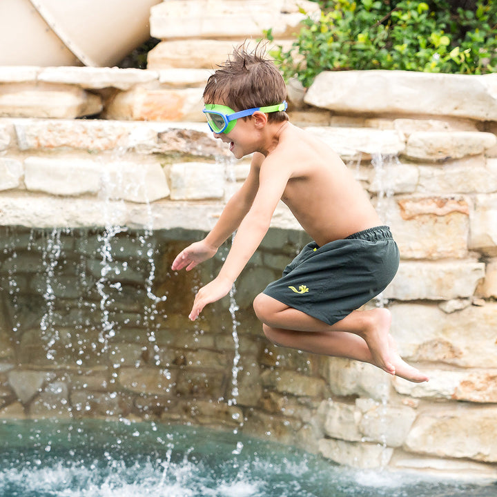 Boy wearing green swim shorts jumping into the pool.