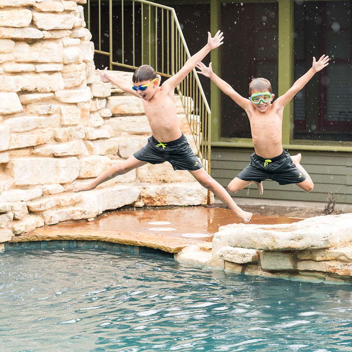 Boys wearing green swim shorts jumping into the pool.