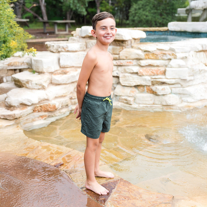 Boy wearing green swim shorts by the pool.