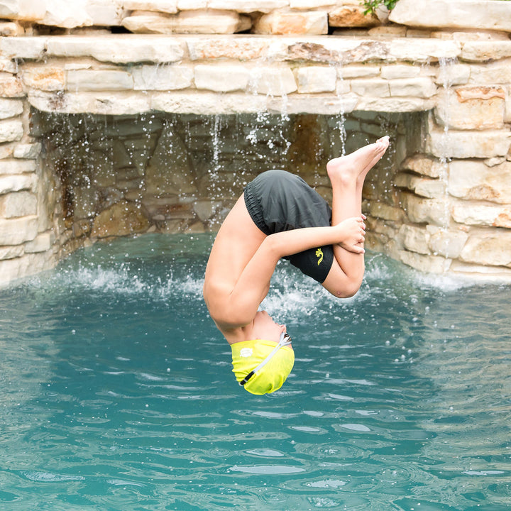 Boy wearing green swim shorts jumping into the pool.