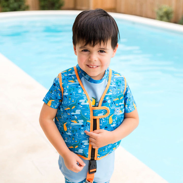 Little one wearing swim vest with non-removable floats in blue, bright orange trims, and crocodiles and frogs themed print. Open.
